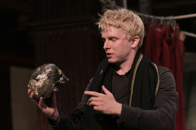 Hamlet in dark shirt and scarf speaks to the blackened skull